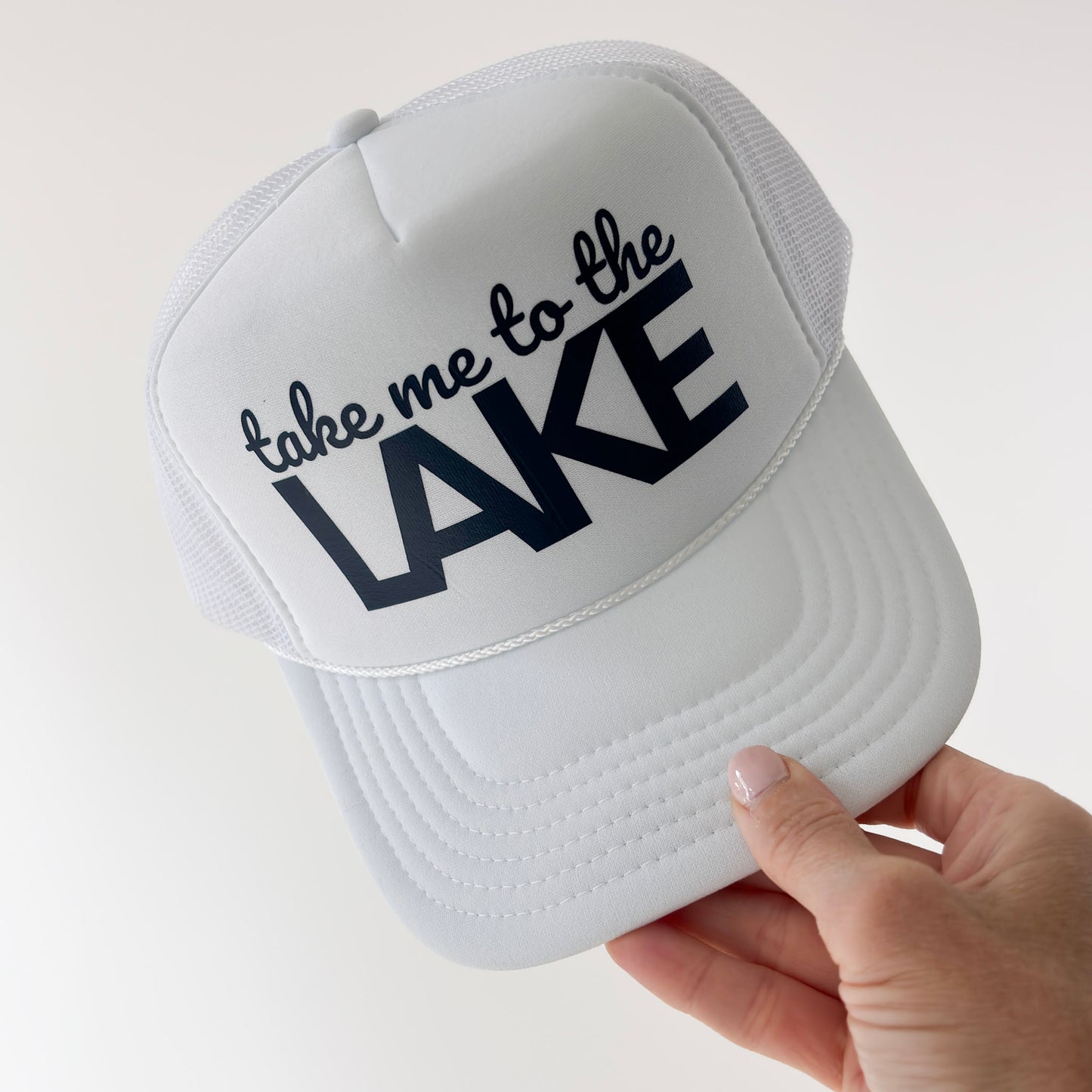 Women's white high profile foam snap back trucker hat with navy blue take me to the lake graphic