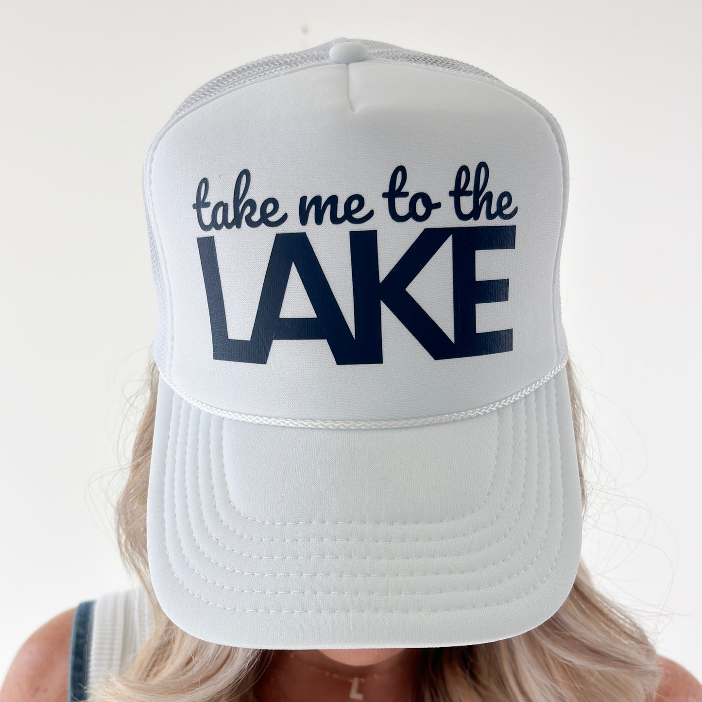 Women's white high profile foam snap back trucker hat with navy blue take me to the lake graphic
